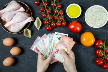 Gıda, avro banknotları, bozuk paralar ve siyah beton arka plandaki ürünler, üst görünüm harcamaları yüksek. 