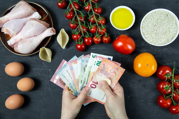 Gıda, avro banknotları, bozuk paralar ve siyah beton arka plandaki ürünler, üst görünüm harcamaları yüksek. 