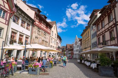 23 Ağustos 2017 Stein Rhein, İsviçre. İnsanlar restoranlarda oturuyor, eski boyanmış binalar ve mavi güneşli gökyüzü.. 