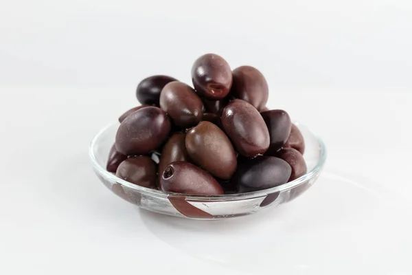 Beyaz arka planda şeffaf bir kasede koyu parlak zeytinler.