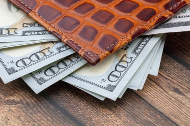 Tahta bir masada deri bir cüzdanda 100 dolarlık Amerikan banknotları. Yakın plan. Bir kırpma yolu kaydedildi.