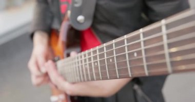 Elektro gitarın tellerine vuran kişi elinde bir pena tutar, kapatır, kamera gitar ensesinden aşağı iner. Prova ya da müzik konseri. Hobi ve eğlence anlayışı