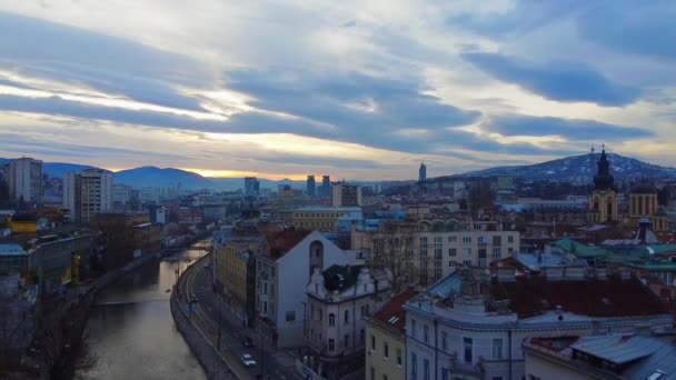 Drona cu aparat de fotografiat coboară peste râu, oferind o vedere spre orașul Saraievo și un drum de-a lungul digului, Bosnia și Herțegovina. Peisaj urban frumos pentru blogul de călătorie — Videoclip de stoc