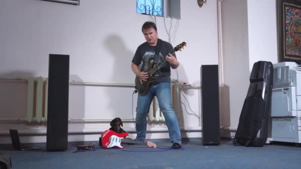 5月25日、ロシア、ロストフ:若い男がエレキギターを演奏し、面白いダックスフンド犬の前で楽器で膝をついて転ぶ。ロックはショーのために新しい曲をリハーサルしている — ストック動画