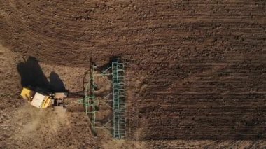 Sarı traktör ilerler ve yeşil bir tarlanın kenarında döner, toprağı gevşetir buğday ekmeye hazırlar, tekerleğin altından toz uçar, üst görüş, drone atışı