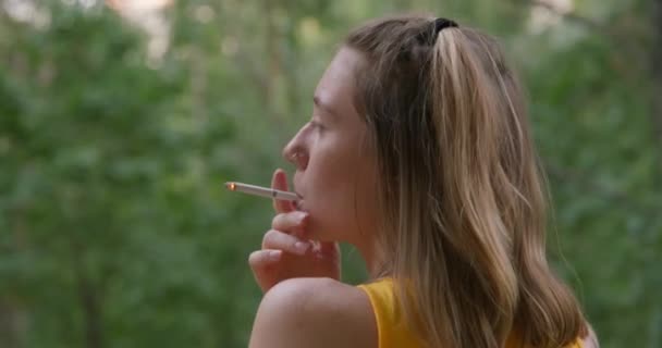 Eine erwachsene junge blonde Frau mit lustiger Frisur schnuppert an einer Zigarette, raucht auf dem Balkon oder illegal auf der Straße, Blick von hinten. Konzept für schlechte Gewohnheiten — Stockvideo