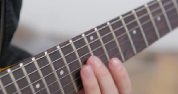 Persona dedos de los trastes a lo largo del cuello y presiona cuerdas, tocando acordes en una guitarra eléctrica, de cerca. Ensayo antes del concierto o aprender a tocar instrumentos musicales — Vídeos de Stock