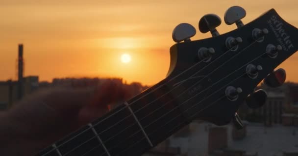 Szeptember 06 2021, Szentpétervár, Oroszország: A személy kézzel igazítja a húrokat, és gitározni kezd. Fejrész elektromos gitárból gépfejjel és ragasztórúddal, közelről — Stock videók