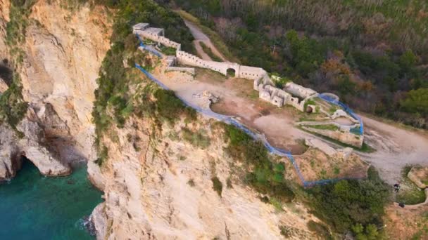 Κάμερα κινείται μακριά από ερείπια του φρουρίου Mogren στην Μπούντβα, που βρίσκεται στην κορυφή του βράχου που πλένεται από τη θάλασσα. Ιστορική αρχιτεκτονική και αρχαιολογικός χώρος περιβάλλεται από ταινία σήματος για την ασφάλεια — Αρχείο Βίντεο