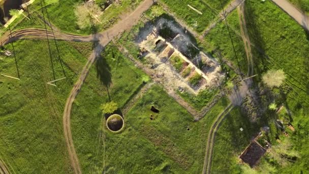 Drone con cámara desciende lentamente sobre un viejo edificio en ruinas, en el que solo quedan paredes con puertas parcialmente, y con pozo de agua rellenado en el patio trasero, pueblo abandonado — Vídeos de Stock