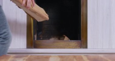 Kişi şömineye şömineyi ısıtmak ve evde rahat bir ortam yaratmak için odun koyar. Soğuk ısıtma mevsiminin başlangıcı. Tatil kavramı