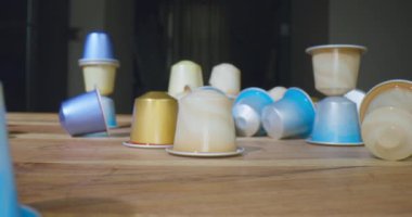 Çeşitli aromalı ve notları olan kapsül kahvesi ahşap masaya saçılmış. Kol dolusu makro çekimde motorlu kamera kaydıracı kullanılarak çekiliyor.