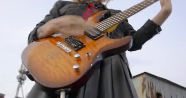 Fiatal szőke rocker bőr szoknyában és dzsekiben energikusan játszik egy elektromos gitáron a szabadtéri koncert alatt, közeli felvétel alulról. Zenei videóklip készítése — Stock videók