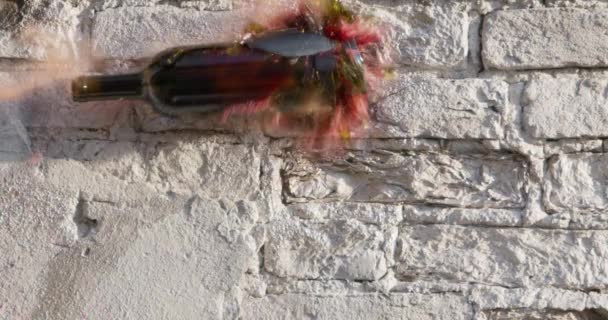 Jemand warf eine Glasflasche Rotwein in eine Ziegelwand, so dass sie zerbrach, Scherben flogen herum und Getränkeflecken auf der Wandoberfläche, Zeitlupe, Nahaufnahme — Stockvideo