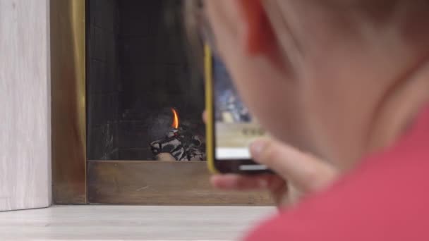 Femme tourne une vidéo verticale sur son téléphone à partager sur les réseaux sociaux. Cheminée classique en pierre avec un bois flamboyant — Video