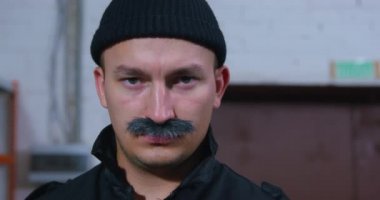 Kalın bıyıklı sert adamın portresi örgü şapkalı ve yakalı siyah ceketli, ciddi ve dikkatli bir şekilde önünde duran, sonra öne eğilip çerçeveden kaybolan