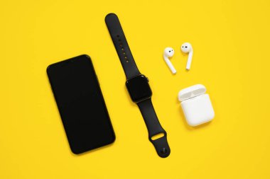 09 Şubat 2021, Rostov, Rusya: Smartphone, Apple watch ve AirPods açık bir çantayla sarı arka plan, üst manzara, reklam metni için kopyalama alanı üzerindedir. Etkin yaşam biçimi için modern aygıtlar