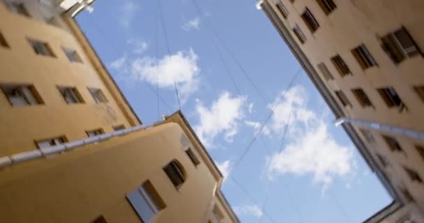 La telecamera gira intorno, rivelando una vista dal basso verso l'alto dei tetti degli edifici di un cortile chiuso, cielo blu con nuvole. Piacevole giornata per una passeggiata turistica in città — Video Stock