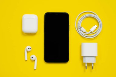2009 Şubat 2021, Rostov, Rusya: Modern akıllı telefon, şarj edilebilir çantalı hava kapsülleri ve güç adaptörlü usb-c-to yıldırım kablosu sarı arka plan, üst görünüm, reklam metni için kopyalama alanı