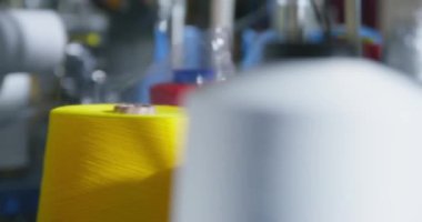 Bir üretim fabrikasındaki robotik makinelere çok renkli iplikli büyük bobinler monte edilir, yakın plan, bulanık ön plan. Dikiş atarken sarı iplik açılır