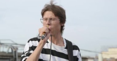 Gözlüklü bir rock 'çının portresi, çatıda altın mikrofonla şarkı söylüyor, saçları rüzgarla darmadağın oluyor. Müzikal açık hava konserinde şarkıcının romantik görüntüsü