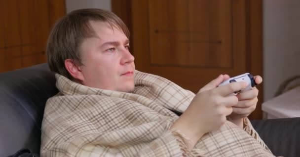 따뜻 한 담요로 둘러 싸인 젊은 남자가 게임을 하고 있습니다. 콘솔을 들고 있는 비디오 게임을 하고 있죠. 누군가 그 의 주의를 빼앗았습니다. — 비디오