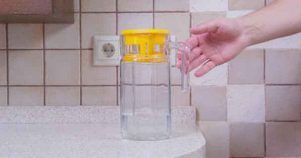 Frau nimmt Wasserfilter mit gelber Kappe, die auf Tisch steht — Stockvideo