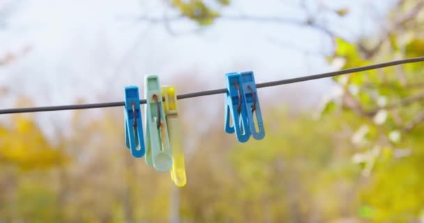 Färgglada klädnypor hänger på järntråd mot gula träd — Stockvideo