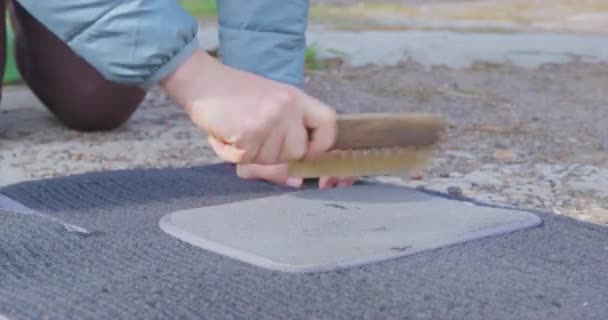 Kadın, sokak zemininde fırçayla araba halısındaki kiri temizliyor. — Stok video