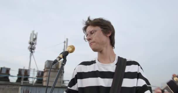 러시아 상트페테르부르크, 2021 년 9 월 6 일: 얼굴에 반짝 이는 화장을 한 젊은 음악가, 실외 쇼나 슈팅 클립을 사용하여, 전자 기타를 가지고 노래의 합창을 풍부하게 부른다 — 비디오