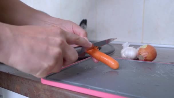 A chef or housewife peels orange carrots with a knife for cooking dinner or lunch — Stockvideo