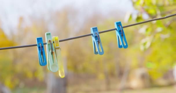 Person takes off clothespins that hang on a rope for drying laundry outdoor, close up, trees covered with green foliage on blurred background. Nice sunny day for household chores — Vídeo de Stock