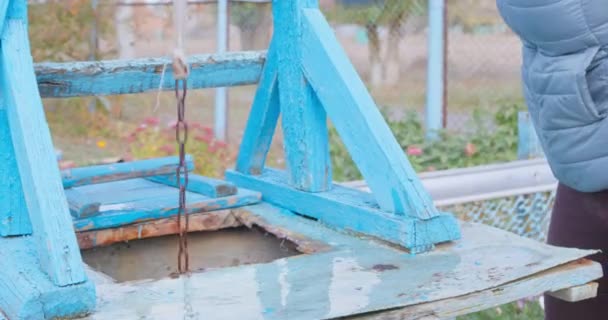 Person lifts bucket of drinking water from well by turning handle of old mechanism. Then person forgot to unfasten bucket from chain, clumsily grabbed it and tried to carry it away, splashing water — Vídeo de Stock