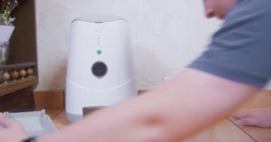 Person removes faulty automatic feeder and drinking machine for pets, and puts in their place the usual ceramic bowls for food and water. Device for feeding dog according to schedule and timer