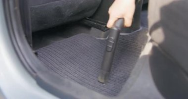 Özel hortumlu elektrikli süpürgeyle arabanın kumaş paspasını dikkatlice süpürür. Araç içi profesyonel temizlik ve kuru temizleme