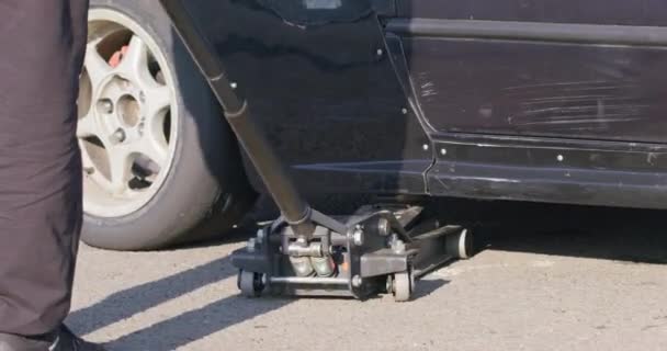 자동차 잭을 사용하여 바퀴를 수리하거나 교체하는 사람들은 낮은 각도에서 볼 수있다. 전문 차량 서비스. 사고의 결과로 현장에서의 교통의 긴급 정비. — 비디오