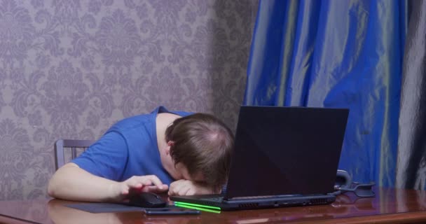 Młody człowiek w niebieskiej koszulce zajmuje się nudną pracą w biurze domowym za pomocą laptopa. Facet ma zły sygnał Wi-Fi, więc wariuje i czeka, aż plik zostanie ściągnięty.. — Wideo stockowe