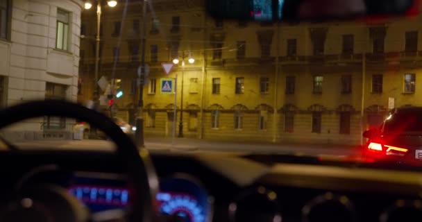 El coche está parado en la carretera en la intersección durante un semáforo rojo, disparando desde el interior desde el asiento trasero del pasajero. Mucho tráfico por la noche en la ciudad. Viaje nocturno por carretera — Vídeos de Stock