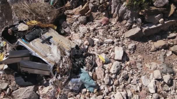 Απομεινάρια πλήρως σπασμένο σκουριασμένο αυτοκίνητο βρίσκονται ανάμεσα σε βράχους, συντρίμμια και ξηρά κλαδιά, drone με κάμερα ανεβαίνει αργά περιστρέφεται γύρω από τον άξονα. Καταστράφηκε όχημα πέταξε από γκρεμό ως αποτέλεσμα ατυχήματος — Αρχείο Βίντεο