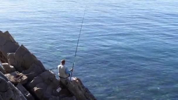 Man enjoys fishing with rod sitting on Adriatic sea rock — Stock Video