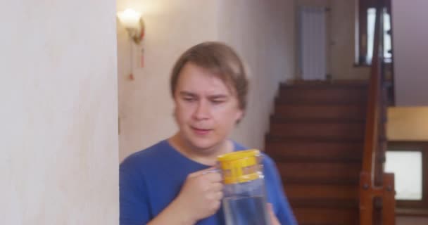 Fussy jongeman in blauw t-shirt rent snel uit de hoek met kruik water. Zenuwachtige man zorgt voor oudere familieleden, kinderen of huisdieren, of water huis planten — Stockvideo