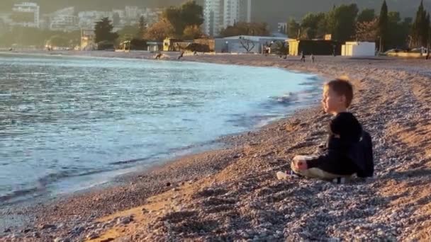 Liten pojke leker på havet stranden med småsten i kuststaden — Stockvideo