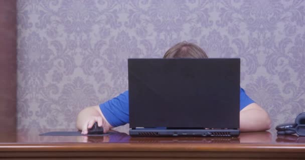 El hombre es duro trabajando o jugando a videojuegos, escondiéndose detrás de la computadora portátil. Alguien le dice al tipo que es demasiado tarde. Mira hacia fuera, comprueba el tiempo en el reloj de pulsera, se sorprende, pero sigue sentado en el ordenador. — Vídeos de Stock