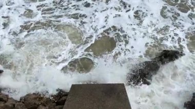 Öfkeli köpüklü dalgalar kayalara çarpıyor ve taşları yıkıyor. Kum fırtınadan dolayı dipten yükseldi, bu yüzden su kirli görünüyor. Doğanın gücü.