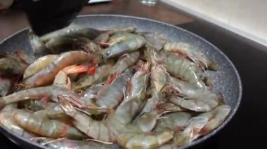 Mutfak spatulası olan kişi karidesleri kızartma tavasında karıştırır. Böylece eşit derecede kızarır, yakın plan. Şenlikli bir akşam yemeği için nefis egzotik yemekler pişiriyorum. Deniz ürünleri menüsü..