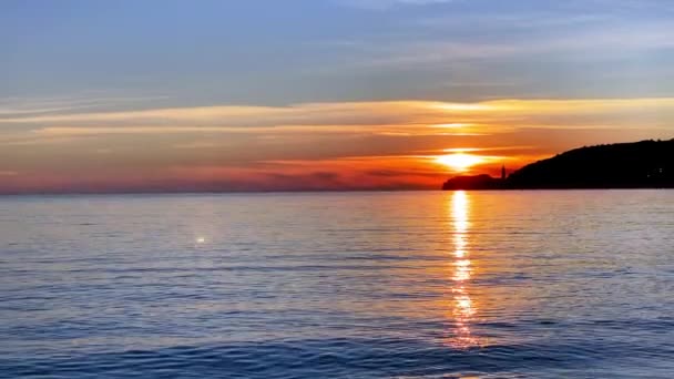 Schilderachtige zeegezicht met verbazingwekkende vurige zonsondergang, panoramisch uitzicht vanaf de kust. Gouden zonnestralen breken door wolken over de berg en kalmeren het zeeoppervlak. Schoonheid der natuur. — Stockvideo
