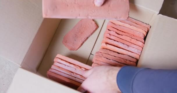 Person begins packing multi-sized tile based on casts of old bricks into cardboard box, laying it tightly in rows. He prepares it to send to retail outlets or to a warehouse for storage, close up. — Stock Video