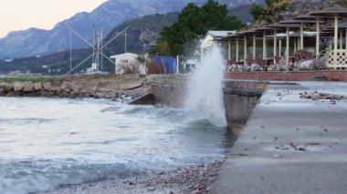 Dalgalar dağların eteklerindeki tatil köyünde kapalı bir kafe önündeki beton setlere çarpıyor. Sıçramalar her tarafa yayılıyor, her yere yayılıyor..