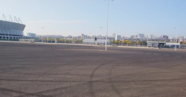 누군가가 자동차, 스쿠터, 자전거, 롤러스케이트를 타고 새로운 스포츠 경기장 근처의 포장된 지역을 운전하고 있습니다. 옥외 활동. — 비디오
