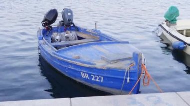 Eski ahşap bir balıkçı teknesi suyun pürüzsüz yüzeyinde yüzer, iskeleye bağlanır, setten manzara seyreder. Deniz aracı iki motorla donatılmış..